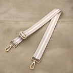 Beige bag strap with gold hardware on a white surface.