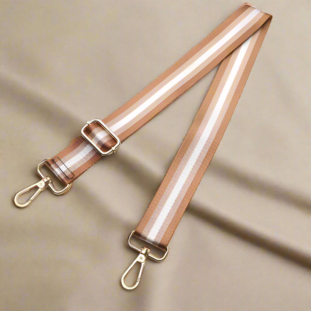 Striped bag strap with gold hardware on a light surface.