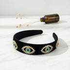 Black headband with eye-shaped embellishments on a white surface