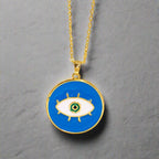 Gold necklace with a blue evil eye pendant on a beige background